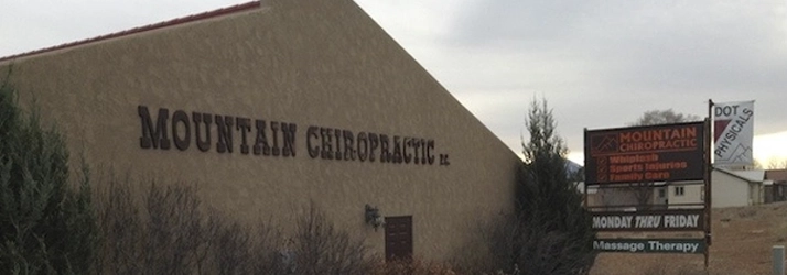 Angled exterior view of a Mountain Chiropractic building with signage, shrubs in the foreground, and overcast sky.