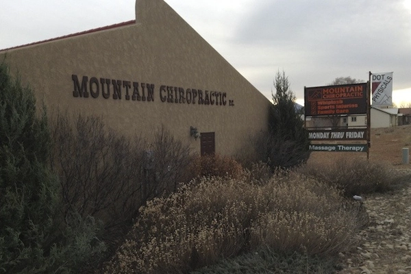 Exterior view of a Mountain Chiropractic building with tan walls, native plants, and a roadside business sign.